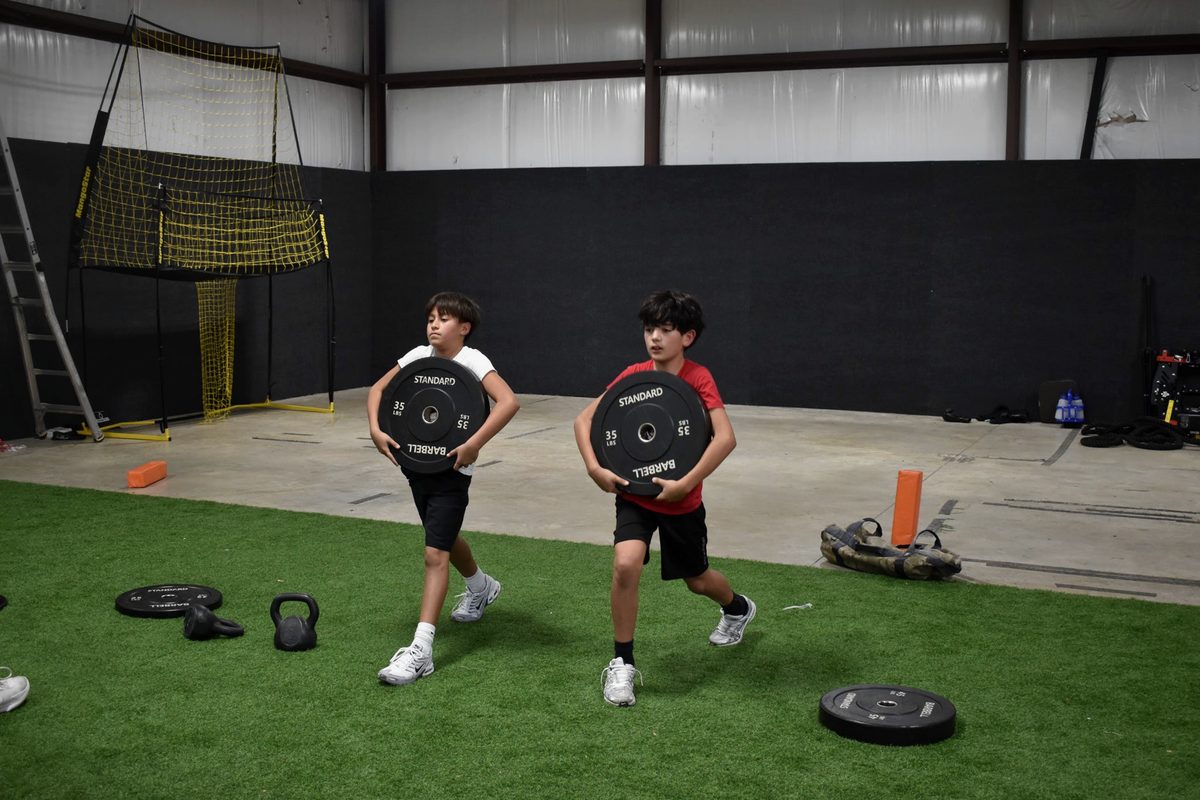 Two students carrying weight plates across the turf during conditioning