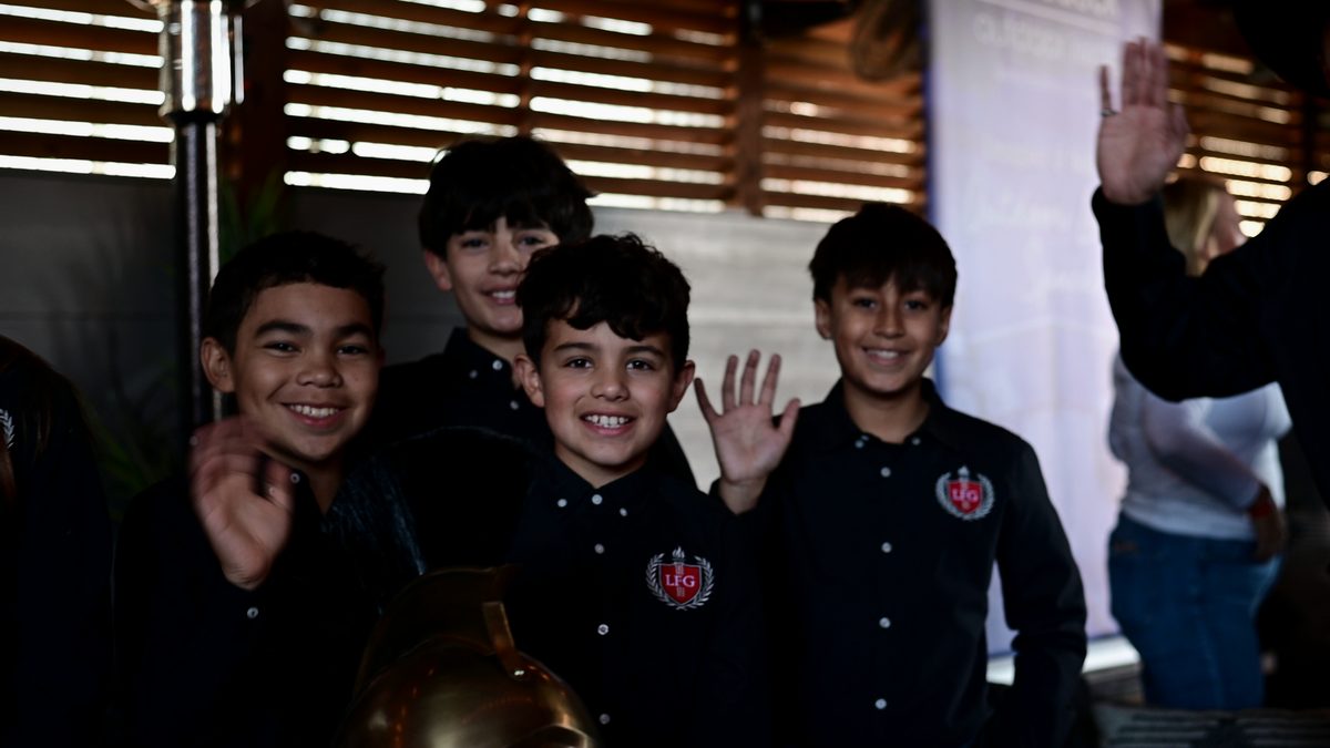Four LFG Academy students smiling and waving at a school event