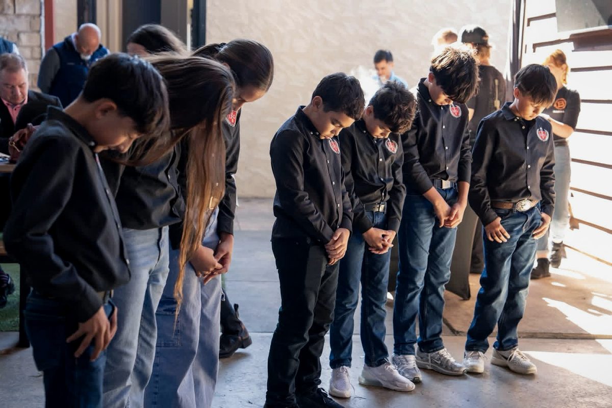 LFG Academy students standing together with heads bowed at a community event