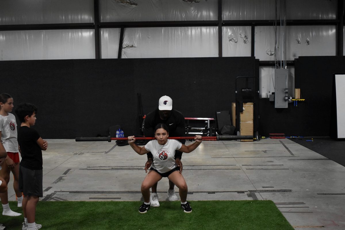 A student working through a barbell squat with a coach spotting